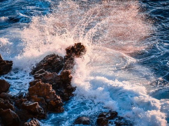 Overhead view of waves breaking on rocks. Credit: Guss B on Unsplash